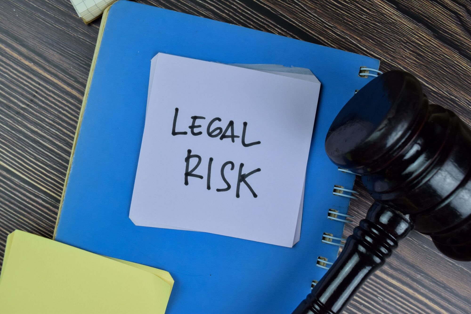 A gavel sits next to a blue file folder with a sticky note reading "Legal Risk."